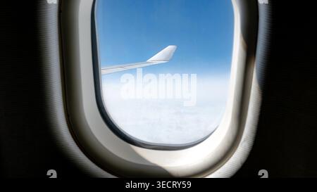 Una vista aerea da una finestra aerea che cattura il cielo blu calmo e le nuvole bianche. L'ala dell'aeroplano è visibile, simboleggiando il viaggio e l'avventura in Th Foto Stock
