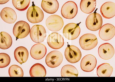 Modello piatto di uva rossa e verde dimezzata, disposte su uno sfondo bianco pulito, che mostra succose fette di frutta e semi, ideale per cibi freschi e s Foto Stock