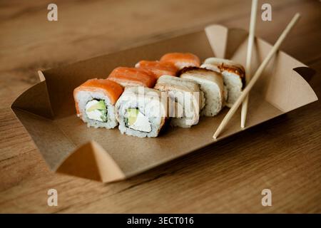 Una scatola da asporto aperta di sushi poggia su un tavolo di legno, con rotoli ordinati all'interno. I rotoli sono accuratamente lavorati e presentati, mostrando il de Foto Stock