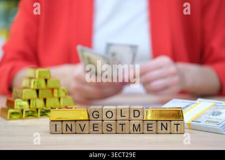 Esplorare il valore dell'investimento in oro con il denaro contante in mano e le scintillanti barre in esposizione Foto Stock
