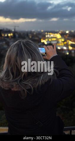 Vista posteriore di una turista che scatta una foto dello skyline di Firenze e di Ponte Vecchio con il suo smartphone al tramonto, Italia. Foto Stock