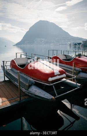 Vista panoramica dei pedalò ormeggiati su un tranquillo lago europeo, con una maestosa montagna sullo sfondo, che invita i viaggiatori a esplorare e abbracciare il Foto Stock