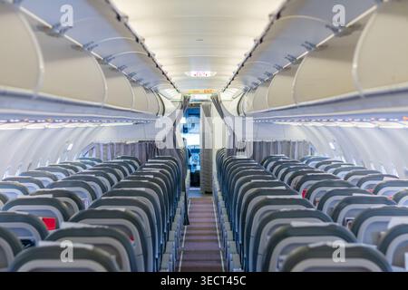 Vista grandangolare in basso nella corsia di una cabina di un aereo commerciale vuota, con file di sedili Economy, cassoni sopra il tetto e illuminazione interna soffusa prima Foto Stock