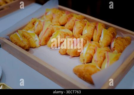 Mini panini con prosciutto e formaggio a croissant disposti su un vassoio di catering in legno per un buffet di hotel. Foto Stock