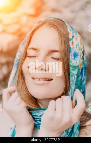 Foulard donna sereno giovane donna con foulard floreale blu sorridente a occhi chiusi in luce soffusa del sole Foto Stock
