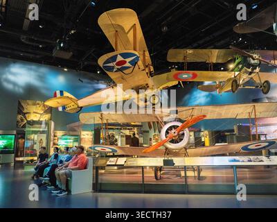 Smithsonian National Air and Space Museum WWI Biplanes Washington DC Stati Uniti | WASHINGTON D.C., Stati Uniti - i visitatori del museo siedono sotto un cammello Sopwith F.1 e altri biplani dell'era della prima guerra mondiale sospesi all'interno dello Smithsonian National Air and Space Museum. Introdotto nel 1917, il caccia britannico è riconosciuto dalla carenatura in metallo ondulato che copre le mitragliatrici Vickers sincronizzate, una caratteristica che ha dato all'aereo il suo nome. Il suo motore rotativo rendeva notoriamente difficile volare ma altamente manovrabile in combattimento. Foto Stock