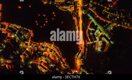 Una splendida vista aerea di un villaggio sul lago di notte, illuminato da calde luci dorate. Lanterne e barche galleggianti creano un modello ipnotico Foto Stock