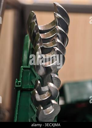 Le lame per trivella in metallo a spirale per primo piano rivelano superfici riflettenti lucide e contrassegni di lavorazione precisi impilati sul supporto verde con profondità ridotta Foto Stock