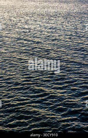 Riflessi dorati sulla superficie del mare durante il tramonto. Consistenza dell'acqua con luce dorata. Foto Stock