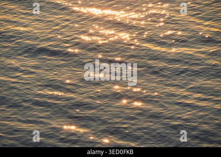 Splendida luce solare dorata che si riflette sulla superficie ondulata del Mar Baltico durante il tramonto, creando una struttura d'acqua scintillante. Foto Stock