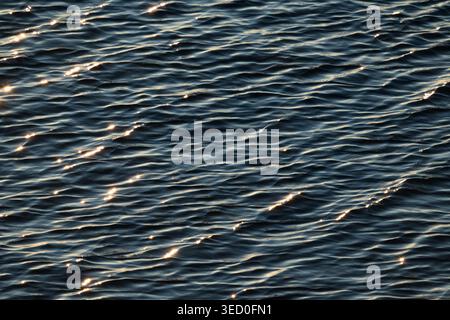 La superficie dell'acqua di mare blu profondo con piccole onde e la luce solare brillante scintilla, la struttura naturale dell'acqua scura del Mar Baltico. Foto Stock
