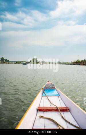 Una prospettiva in prima persona dalla prua di una tradizionale barca shikara in legno, scivolando attraverso le calme acque ondulate del lago dal a Srinagar, Kashmi Foto Stock
