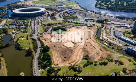 Un grande cantiere si snoda vicino a un vivace stadio, circondato da vegetazione lussureggiante e da un fiume tortuoso. Le macchine sono impegnate a rimodellare la terra, Mark Foto Stock