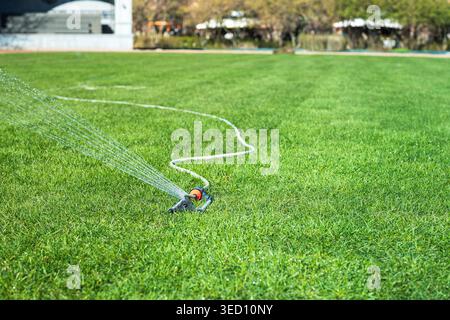 Innaffiatura automatica del prato con impianto sprinkler nelle giornate di sole. Irrigazione, irrigazione di erba verde per la crescita Foto Stock
