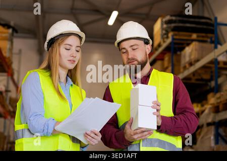 Dipendenti di logistica maschili e femminili che esaminano la scatola bianca con i documenti per la verifica. Primo piano dell'ispezione di qualità e valutazione del prodotto nel centro di distribuzione Foto Stock