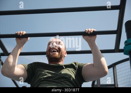 Il bell'uomo fa i pull-up sul bar orizzontale in strada sul campo sportivo. All'aperto. Estate. Allenamento. Routine mattutina. Foto Stock