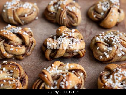 Ambiente accogliente di cottura - nodi di cannella svedesi appena sfornati (kanelbullar) disposti su un tagliere di legno Foto Stock