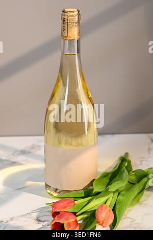 Una bottiglia di vino bianco si stende accanto ai tulipani su marmo. Foto Stock