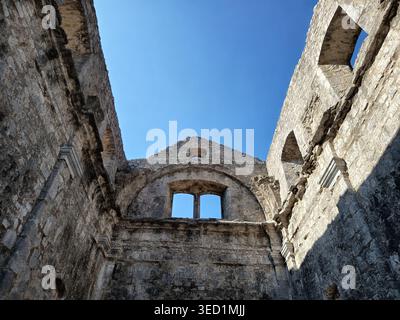 Guardando in alto le pareti in pietra e gli archi vuoti delle finestre di un antico edificio in rovina contro un cielo azzurro. Foto Stock