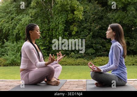 Diverse amiche in abbigliamento sportivo sedute a meditare con mudra su tappetini da yoga sul patio in mattoni Foto Stock