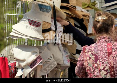 Una donna sfoglia una variopinta selezione di cappelli in un vivace mercato. Kiev, Ucraina 3 maggio 2026. Fiera dell'artigianato popolare ucraino. Foto Stock
