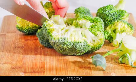 Coltello che taglia le fioriture di broccoli su un asse di legno durante la preparazione. Foto Stock