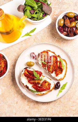 Toast con formaggio spalmabile e pomodori secchi. Aprire il panino con rucola, pane, pomodori, olive e olio. Foto Stock