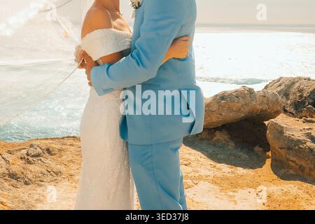 La coppia celebra il matrimonio sull'oceano al tramonto con le onde sullo sfondo. la coppia si trova sulla costa rocciosa per godersi il giorno del matrimonio. il sole tramonta sul Foto Stock