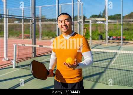 Uomo asiatico che gioca a Pickleball tenendo paddle e palla Foto Stock