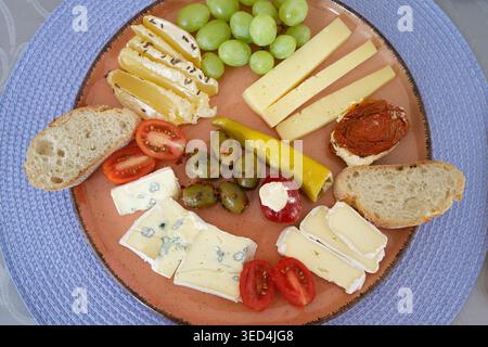 Un appetitoso tagliere di formaggi con formaggio blu, camembert, uva, olive, pomodori, e pane fresco su un piatto di terracotta Foto Stock