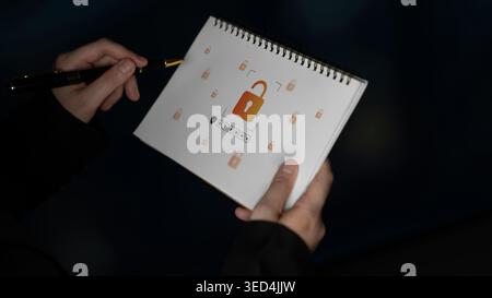 Un individuo concentrato ha un notebook a spirale con un'icona a forma di lucchetto, che simboleggia la sicurezza e la privacy nel mondo digitale. L'immagine acquisisce Foto Stock
