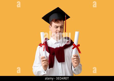 Studente maschile in bacheca con diplomi su sfondo giallo Foto Stock