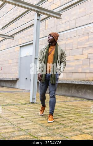 Uomo afroamericano che cammina attraverso il cortile piastrellato sotto il baldacchino con foulard e bomber Foto Stock