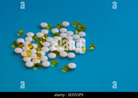 Pile di compresse bianche e capsule gel gialle su sfondo blu, salute e concetto di integratore con spazio di copia, composizione minima studio. Foto Stock