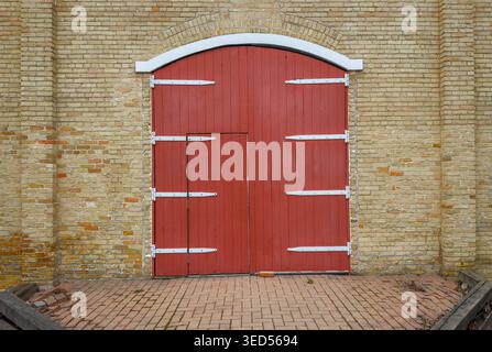 Porte in legno rosso vintage con cerniere in metallo incastonate in un vecchio muro di mattoni gialli, sfondo architettonico rustico con composizione simmetrica e textu Foto Stock