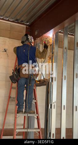 Il lavoratore edile salda prigionieri metallici in interni con scintille e dispositivi di protezione in un cantiere di Los Angeles Foto Stock