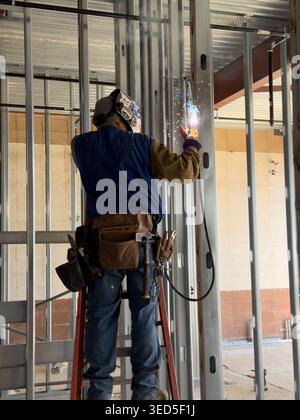 Il lavoratore edile salda prigionieri metallici in interni con scintille e dispositivi di protezione in un cantiere di Los Angeles Foto Stock