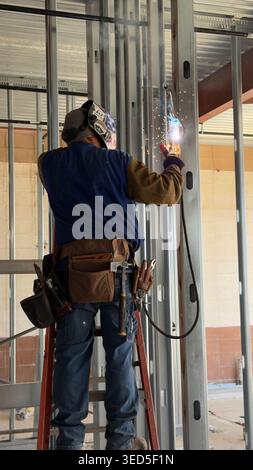 Il lavoratore edile salda prigionieri metallici in interni con scintille e dispositivi di protezione in un cantiere di Los Angeles Foto Stock