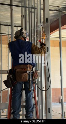 Il lavoratore edile salda prigionieri metallici in interni con scintille e dispositivi di protezione in un cantiere di Los Angeles Foto Stock