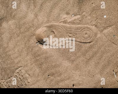 Primo piano dettagliato di un'impronta di scarpe impressa nella sabbia della spiaggia. La texture naturale e la composizione minimale creano un'immagine forte per i viaggi e le attività all'aperto Foto Stock