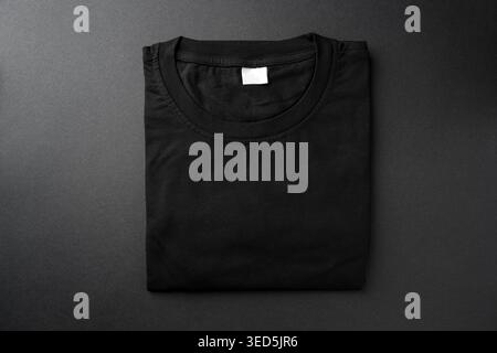 T-shirt nera ripiegata su sfondo scuro per un mockup di abbigliamento Foto Stock