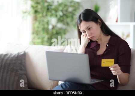 Annoiata donna asiatica che aspetta per molto tempo a pagare online con carta di credito e laptop a casa Foto Stock