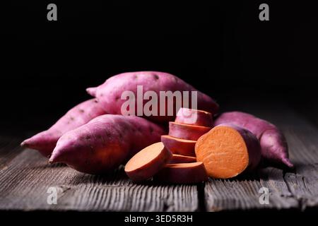 Patate dolci con pezzi tagliati su un tavolo di legno. Cibo vegetale biologico sano Foto Stock