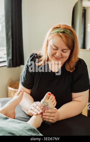 Terapista sorridente che fa massaggio ai piedi, unghie dei piedi dipinte di rosso Foto Stock
