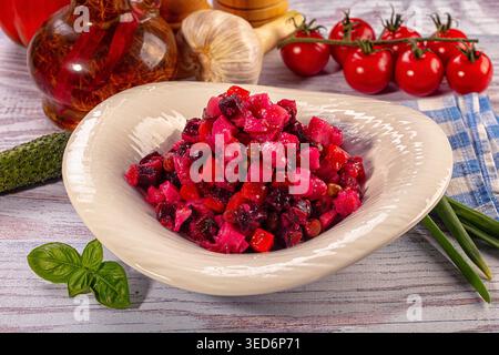 Primo piano di insalata di barbabietole rosse, vinaigrette classica, in un recipiente bianco. Ambiente rustico con ingredienti freschi come aglio, pomodori ed erbe aromatiche Foto Stock