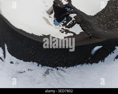 Veduta aerea del bordo del cratere vulcanico sul lato sud dell'Etna con cenere nera, macchie di neve bianca e un escursionista in piedi sul bordo di Nicol Foto Stock