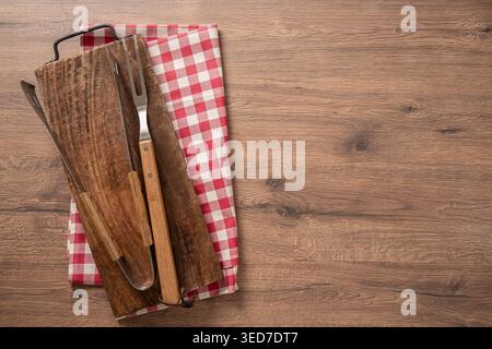Utensili per barbecue su tavola di legno con ampio spazio per le copie su un tavolo di legno, vista sullo sfondo rustico del barbecue per il concetto di griglieria e pubblicità estiva Foto Stock