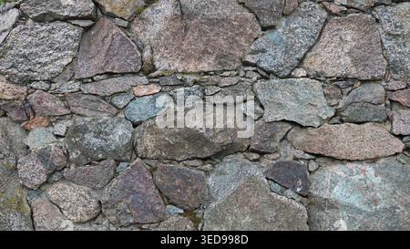 Bella pietra ruvida fatta di massi di granito e piccoli ciottoli, un frammento di un muro o di una recinzione di roccia naturale, la consistenza della pietra Foto Stock