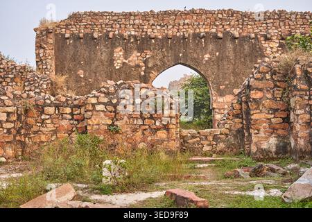 Antiche rovine di pietra consumate dal tempo con muri in muratura marrone-rossastro e un'imponente porta ad arco nello sfondo centrale. La struttura presenta Foto Stock