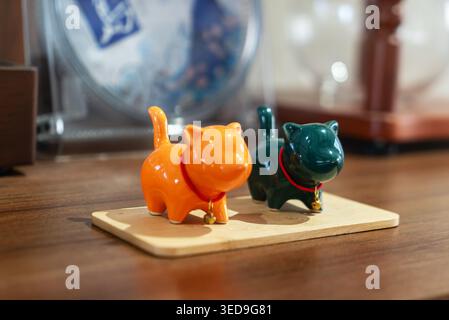 Due statuette in ceramica a forma di gatto, una arancione e una verde scuro, sono esposte su una piccola tavola di legno, aggiungendo un tocco giocoso e affascinante a casa o. Foto Stock